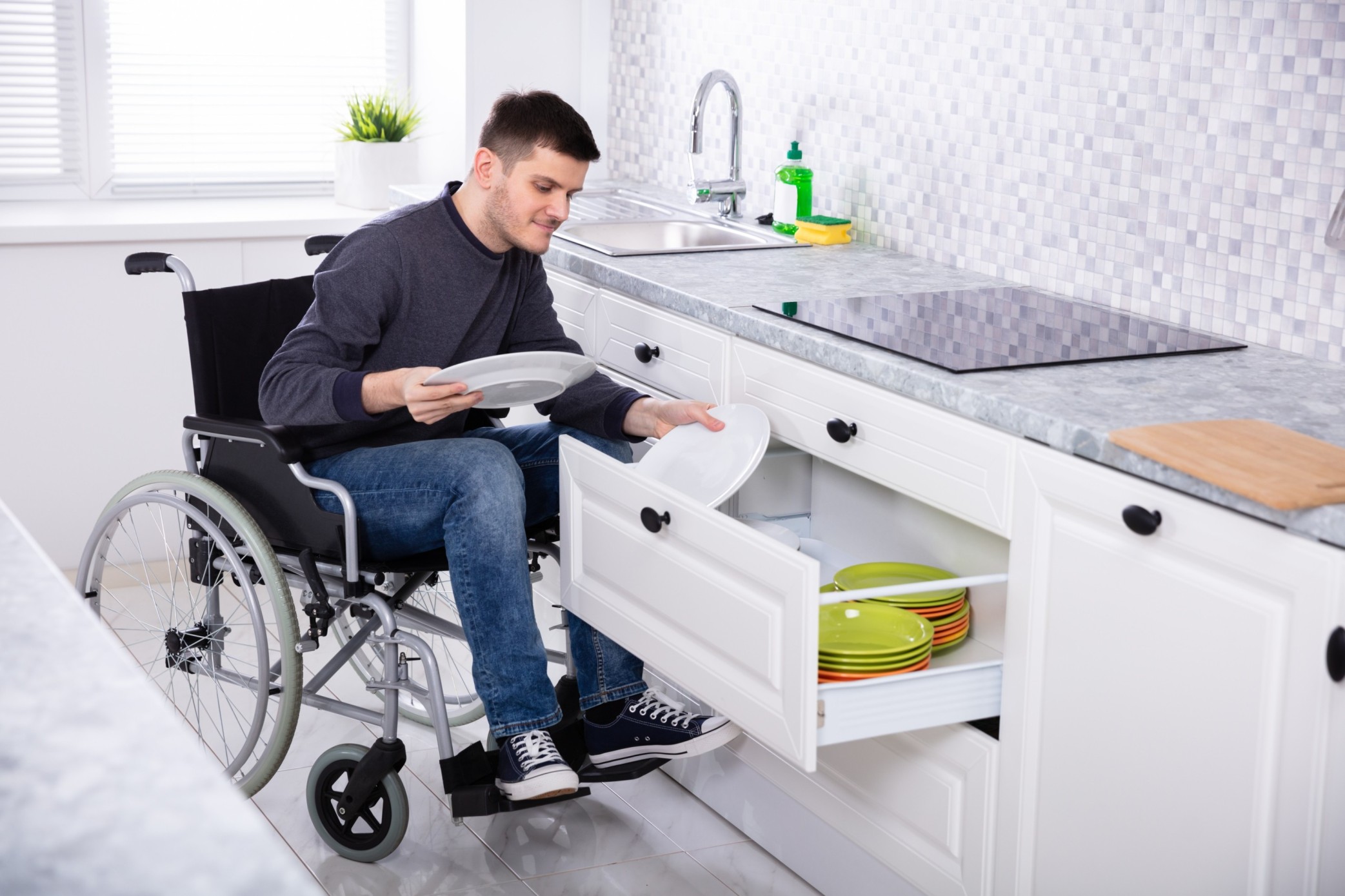 Disabled man in wheelchair in kitchen using drawer